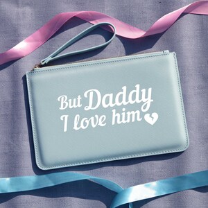 May include: A light blue zippered pouch with a white leather strap. The pouch has the text "But Daddy I love him" in white lettering with a small white heart.