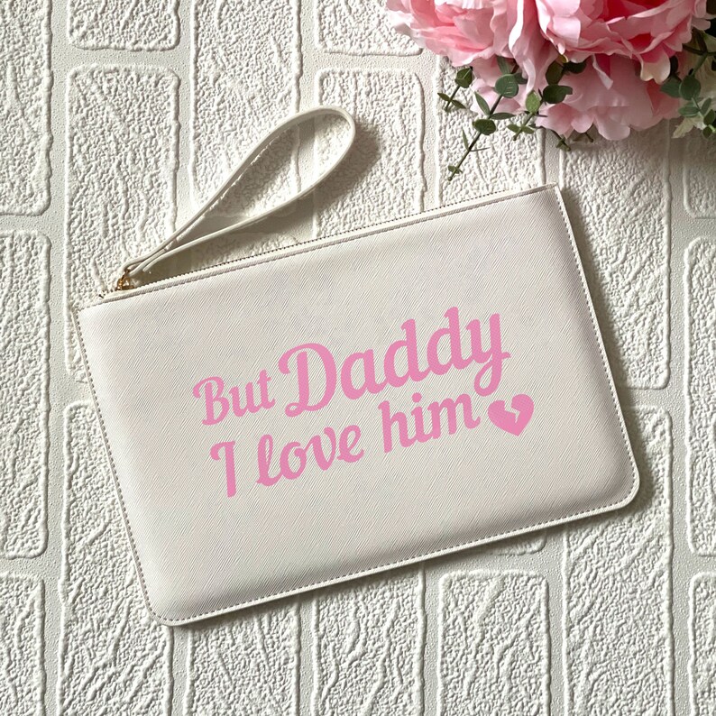 May include: White clutch bag with a pink inscription that reads "But Daddy I love him" with a pink heart.