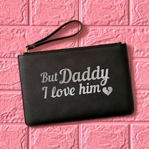 May include: Black clutch bag with a zipper closure and a silver handle. The bag has the text "But Daddy I love him" with a broken heart symbol.