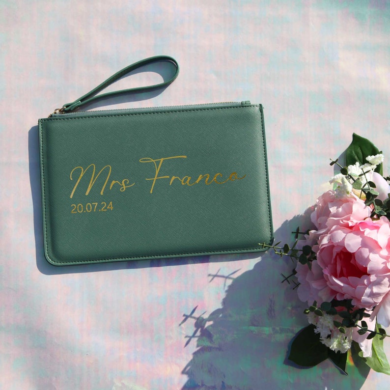 May include: A green clutch purse with a gold zipper and a gold inscription that reads "Mrs. Franca 20.07.24".