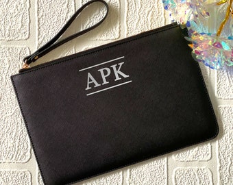 May include: Black clutch bag with a zipper closure and a wrist strap. The bag has the initials "APK" printed in white on the front.