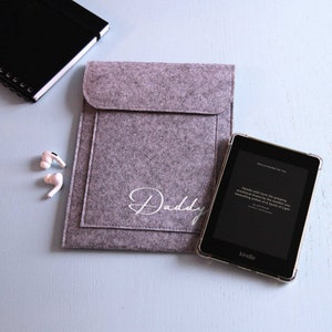 May include: A gray felt tablet sleeve with the word "Daddy" embroidered in white. A black Kindle e-reader is next to the sleeve.