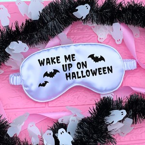 May include: White satin sleep mask with black text that reads "Wake Me Up On Halloween" and black bat silhouettes.