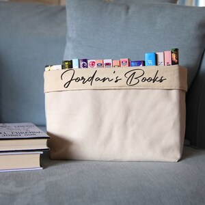 May include: A white canvas book storage bin with the text "Jordan's Books" printed on the front. The bin is filled with a variety of colorful books.