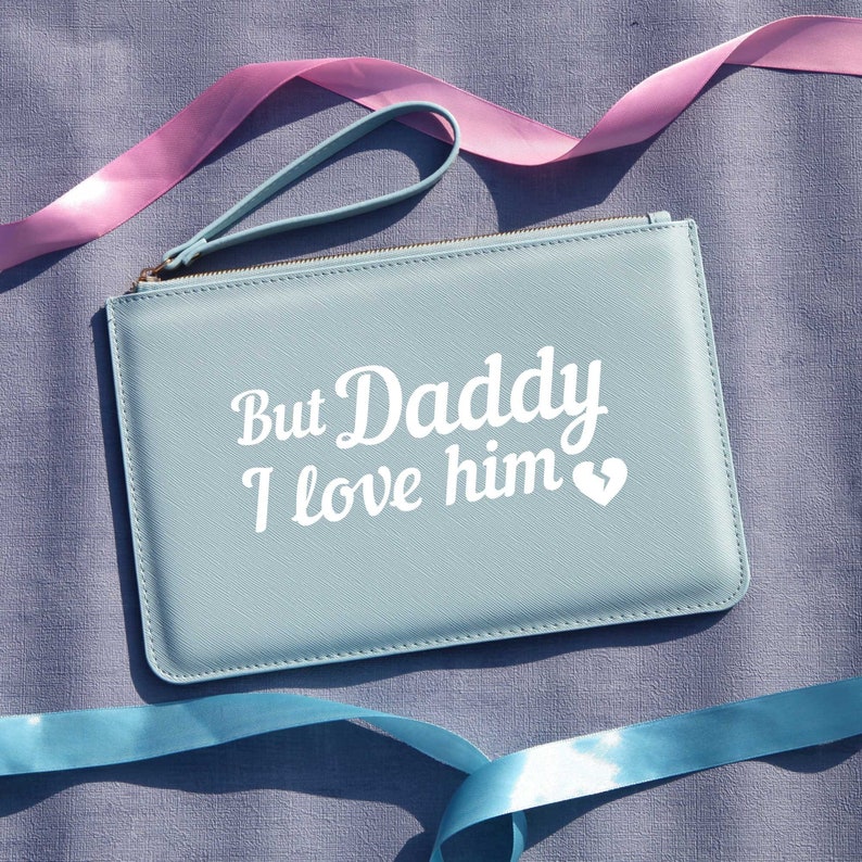 May include: A light blue zippered pouch with a white leather strap. The pouch has the text "But Daddy I love him" in white lettering with a small white heart.