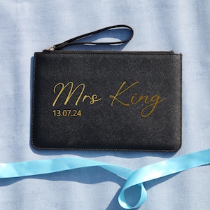 May include: Black clutch bag with a gold zipper and a gold inscription that reads "Mrs King 13.07.24".