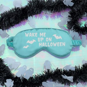 May include: A turquoise blue sleep mask with the text "Wake Me Up On Halloween" and a white bat design.