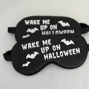 May include: Two black sleep masks with white text and bat silhouettes. The text reads "Wake me up on Halloween".
