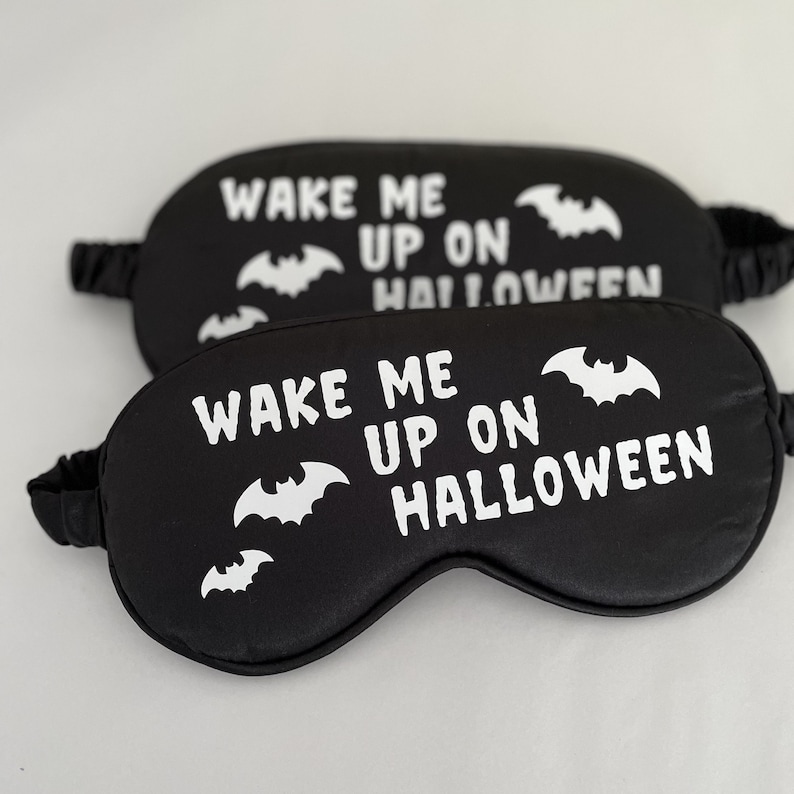 May include: Two black sleep masks with white text and bat silhouettes. The text reads "Wake me up on Halloween".