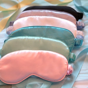 May include: Six silk sleep masks in various colours, including light blue, turquoise, pink, and white. The masks are arranged in a stack, with the pink mask on top.