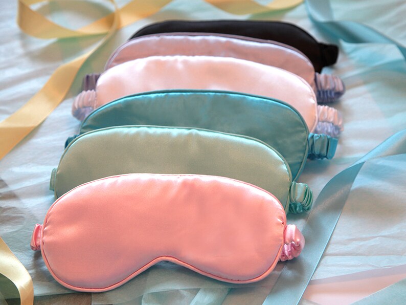 May include: Six silk sleep masks in various colours, including light blue, turquoise, pink, and white. The masks are arranged in a stack, with the pink mask on top.