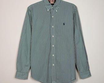 May include: A long-sleeve button-down shirt featuring a vertical pinstripe pattern in shades of green, white, and navy blue. The shirt has a pointed collar with button-down points, a central button placket, and a small dark blue embroidered logo.