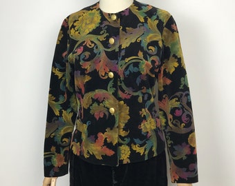 Könnte beinhalten: Schwarze Samtjacke mit farbenfrohem Blumenmuster in Gelb-, Grün-, Orange- und Lilatönen. Die Jacke hat einen runden Kragen, lange Ärmel und goldene Knöpfe. Ein klassischer Vintage-Stil.