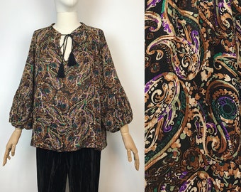 May include: A brown, green, and purple paisley print blouse with a tie at the neck and long, puffed sleeves.