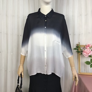 Pode incluir: Uma camisa de botões com ombre branco e preto com um único bolso do lado esquerdo. A camisa tem um caimento solto e é feita de um tecido leve.