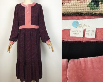 May include: A long-sleeved, burgundy midi dress with a pink velvet trim around the neckline, cuffs, and waist. The dress has a floral print and a tiered skirt. The dress is made in China and is size UK 12R, US 8R. The label reads "Boden".
