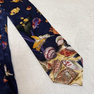 May include: Navy blue necktie featuring a marine life design. The tie showcases a variety of sea creatures, including sea turtles, fish, and seashells. The design incorporates shades of yellow, orange, red, and white, creating a vibrant and detailed pattern.