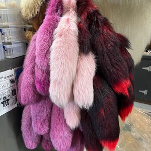 May include: A collection of fox tails in various shades of pink and red. The tails are arranged in a bundle and are hanging from a hook.