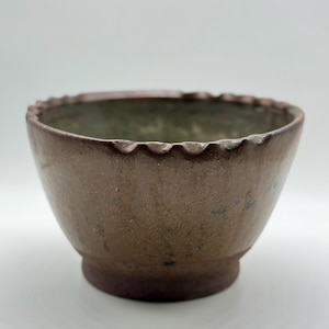 May include: A handmade, brown ceramic bowl with a scalloped rim. The bowl has a wide opening and a slightly textured surface. The base is a darker shade of brown. The bowl is likely used for serving food or as a decorative piece.