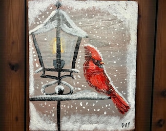 May include: A painting of a red cardinal perched on a black wrought iron lamp post in a snowy scene. The lamp has a lit yellow light. The background is a muted gray with white snowflakes.
