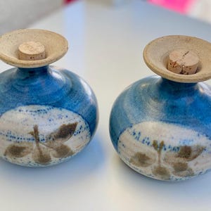 Puede incluir: Dos saleros y pimenteros de cerámica azul con tapones de corcho y un diseño floral blanco y marrón.