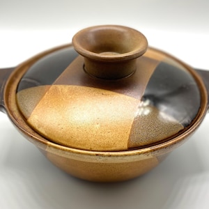 Op de afbeelding: Een bruine en zwarte keramische ovenschaal met een deksel. De schaal heeft een geometrisch patroon en een licht verhoogde rand.