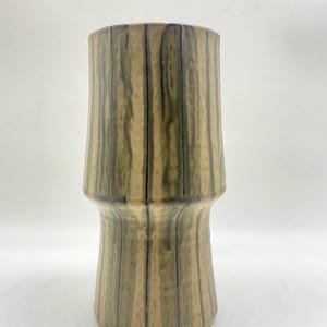 May include: A tall, handmade ceramic vase with a cylindrical shape. The vase features vertical stripes in shades of green, tan, and black. The vase has a flared base and a slightly wider top, standing approximately 10 inches tall.