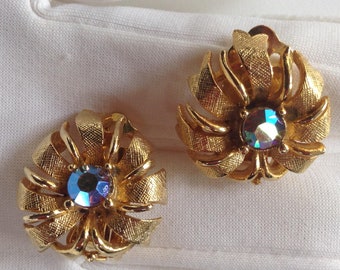 May include: A pair of gold tone clip-on earrings with iridescent blue stones in the center of each flower-shaped design.