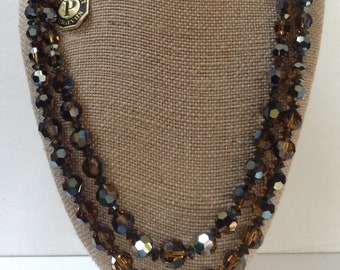 May include: A multi-strand necklace made of dark brown and black faceted glass beads. The necklace is displayed on a brown fabric mannequin.