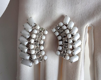 May include: A pair of vintage clip-on earrings. Each earring features a curved design with white rectangular and round stones, accented with smaller clear rhinestones. The earrings are set on a silver-tone metal backing.