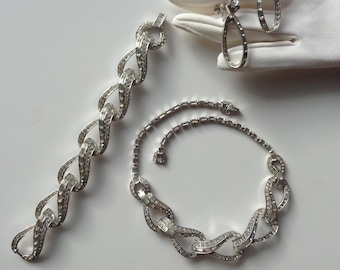 May include: A set of silver tone jewelry featuring a necklace, bracelet, and earrings. The pieces are made of linked chains with clear rhinestones.