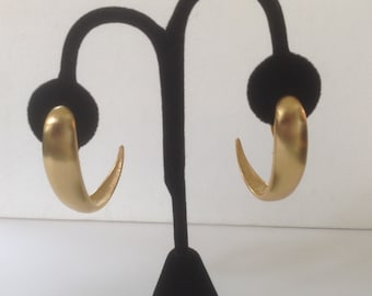 May include: A pair of gold hoop earrings with a smooth, rounded finish. The earrings are displayed on a black stand.