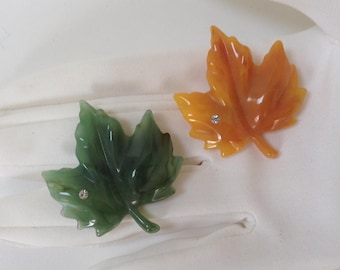 May include: Two maple leaf brooches, one green and one orange, with a rhinestone accent on each.