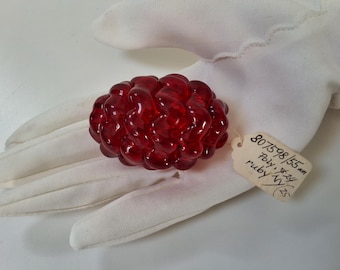 May include: A translucent, ruby-red glass object with a textured, organic shape, possibly a decorative piece. The object rests on a white surface, with a small tag attached. The tag has handwritten text including the word "ruby".
