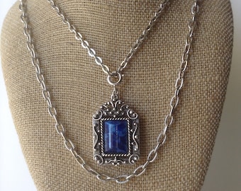 May include: A silver chain necklace with a pendant featuring a blue gemstone set in a silver frame with ornate details.
