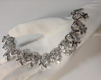 May include: A silver necklace with a chain made of interlocking heart-shaped links. Each link is decorated with a delicate criss-cross pattern.