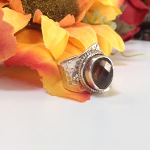 May include: A silver ring with a large, faceted, dark brown gemstone. The ring has a textured band and intricate details around the stone.