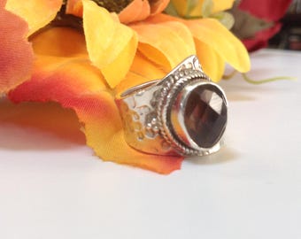 May include: A silver ring with a large, faceted, dark brown gemstone. The ring has a textured band and intricate details around the stone.