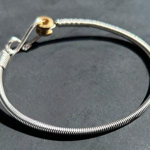 May include: A silver guitar string bracelet with a gold clasp.