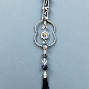 May include: A silver-toned guitar-shaped charm with a clear crystal and black beads, and a black tassel. The charm is suspended from a black cord. The guitar shape is made of wire.