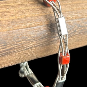 May include: A silver guitar string bracelet with red and black square beads.