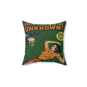 Puede incluir: Una almohada verde y naranja con un diseño de portada de cómic vintage. La portada presenta a una mujer atrapada en una telaraña con una araña con cabeza de calavera. El texto de la portada dice "Adventures into the Unknown!" y "World's Greatest Supernatural Stories."