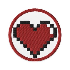 May include: A red pixelated heart embroidered on a white circle with a red border.