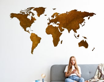 May include: A woman sits on a gray couch in front of a white wall with a large, brown world map cutout. She is looking at her phone and has long blonde hair.