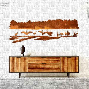 K&ouml;nnte beinhalten: Ein Wandbild aus Metall, das eine Vogelschar darstellt, die &uuml;ber eine Waldszene fliegt. Die Kunst ist aus rostigem Metall gefertigt und hat eine braune und orangefarbene Farbgebung. Das Kunstwerk ist an einer wei&szlig;en Wand &uuml;ber einer Kommode aus Holz angebracht.
