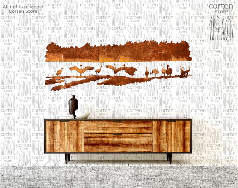 K&ouml;nnte beinhalten: Ein Wandbild aus Metall, das eine Vogelschar darstellt, die &uuml;ber eine Waldszene fliegt. Die Kunst ist aus rostigem Metall gefertigt und hat eine braune und orangefarbene Farbgebung. Das Kunstwerk ist an einer wei&szlig;en Wand &uuml;ber einer Kommode aus Holz angebracht.