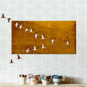 May include: A rectangular metal wall art piece with a rustic, orange-brown finish. The art features a flock of white birds flying in a V-formation against a textured background. The art is displayed on a white wall with a repeating pattern of vertical lines.