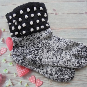 May include: Black and white knitted socks with a black cuff featuring white polka dots. The cuff has a textured, puffy look.