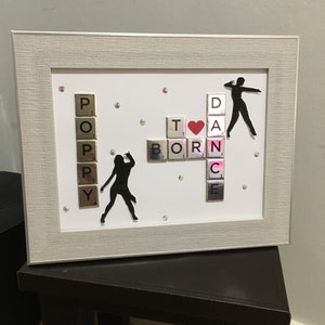 May include: A framed white background with black silhouettes of dancers and the words "BORN TO DANCE" spelled out with Scrabble tiles. A red heart is placed between the words "TO" and "DANCE".