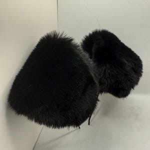 May include: Two black fur earmuffs are displayed against a white background. The earmuffs are fluffy and appear to be made of faux fur. The ear coverings are connected by a thin, black band.